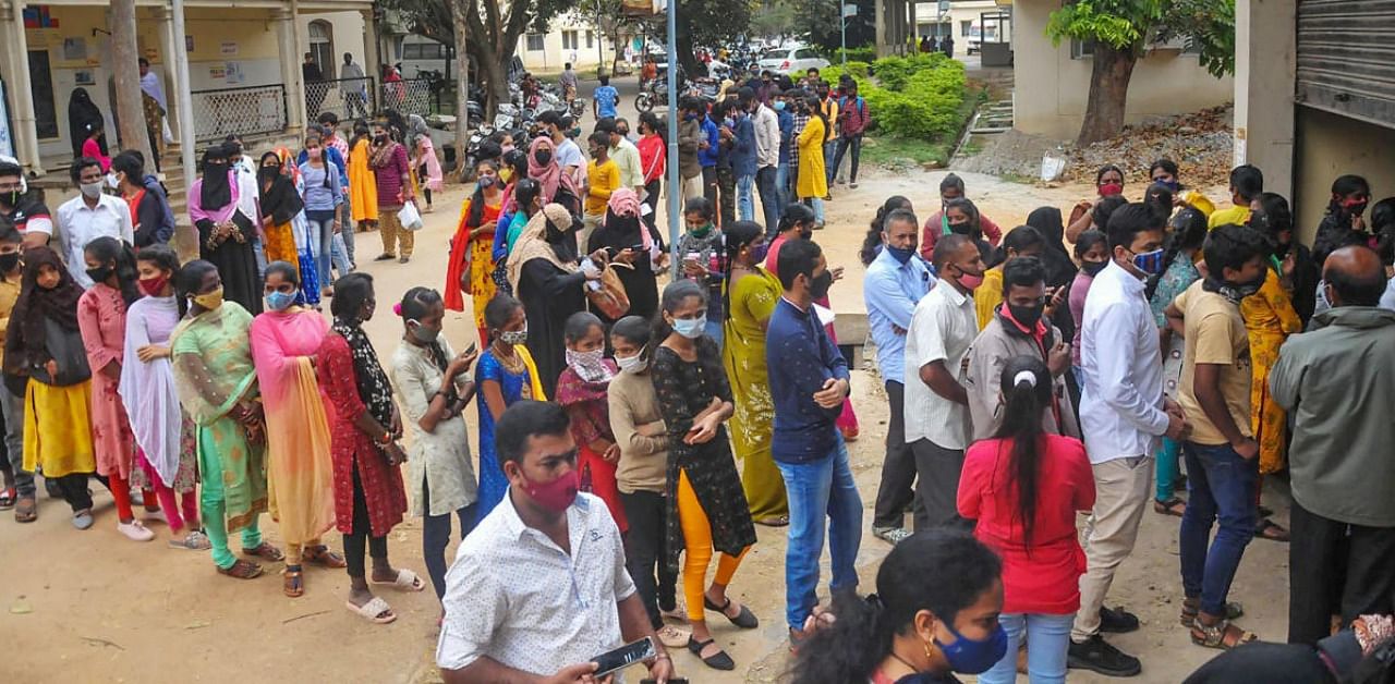 People stand in queues as they wait for their turn to give samples for Covid-19 test, at a centre in Chikmagalur. Credit: PTI.
