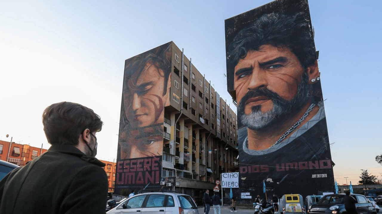 People gather at the foot of a mural of late Argentinian football legend Diego Maradona (R) in Naples, southern Italy, to mourn his death. Credit: AFP File Photo