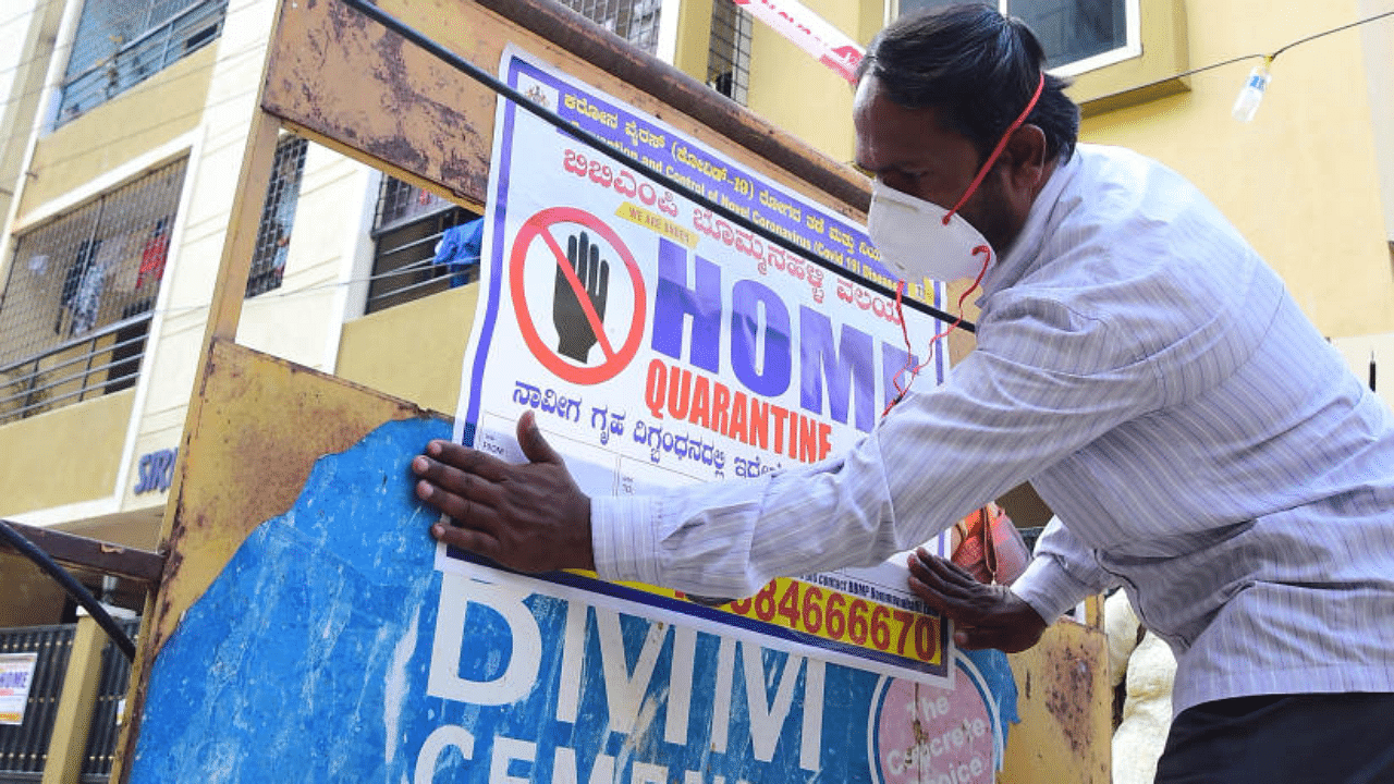 A BBMP worker on Wednesday puts up a poster on a barricade outside the apartment in Kumaraswamy Layout, Bengaluru, where the UK returnees who tested positive for the new strain live. Credit: DH Photo