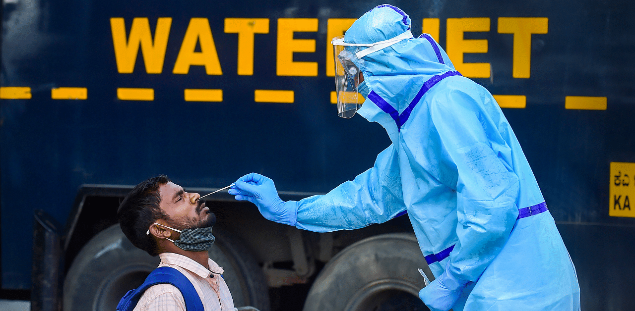 A health worker collects swab sample of a passenger for the Covid-19 test at the KSRTC bus stand in Bengaluru. Credit: PTI