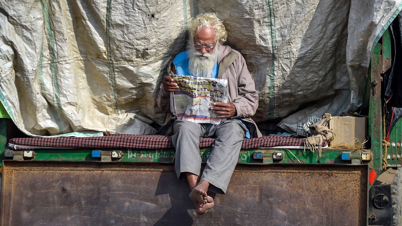 A farmer reads a newspaper during a protest against the new farm laws, at Singhu Border in New Delhi. Credit: PTI Photo