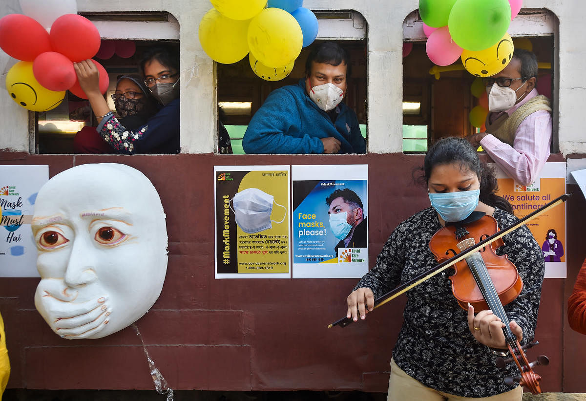 Passengers listen to an artist playing violin outside a tram during an awareness campaign against coronavirus, on the New Year's eve, at Esplannade Tram depot in Kolkata. Credit: PTI. 
