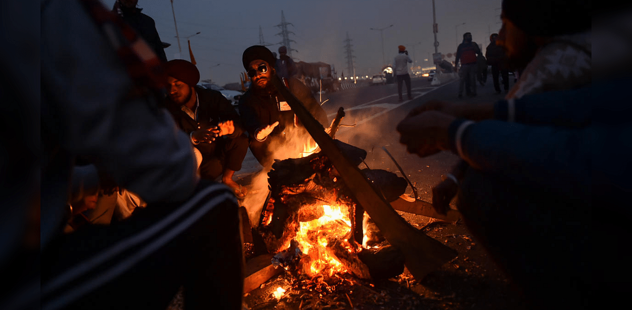 Farmers sit around a bonfire to keep themselves warm during their ongoing agitation against the farm reform laws. Credit: PTI Photo