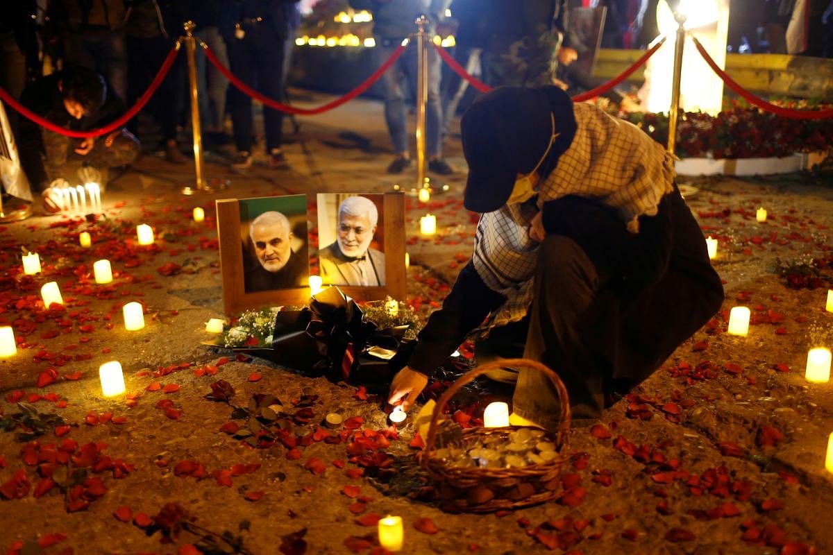A person lights a candle near pictures of senior Iranian military commander General Qassem Soleimani and Iraqi militia commander Abu Mahdi al-Muhandis on the first anniversary of their killings in a U.S. attack, in Baghdad, Iraq, January 2, 2021. Credit: REUTERS Photo
