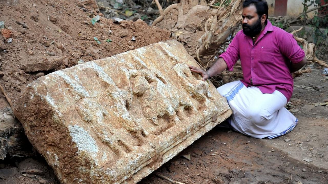 Jalakanteshwara temple chief priest Mohan Dixit takes a look at a stone carving depicting Shiva and Parvathi that was unearthed in Kalasipalya last week. Credit: DH photo/Pushkar V.