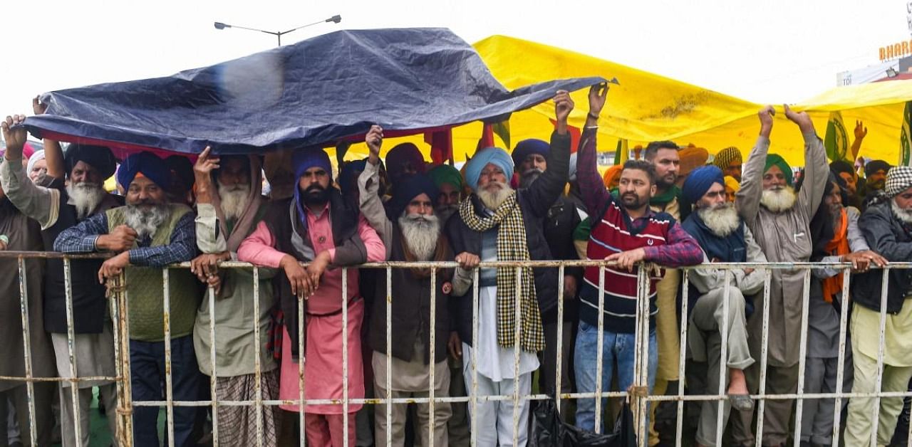 Farmers take cover from the rain during their ongoing protest against new farm laws, at Singhu border, in New Delhi, Monday, Jan. 4, 2021. Credit: PTI Photo