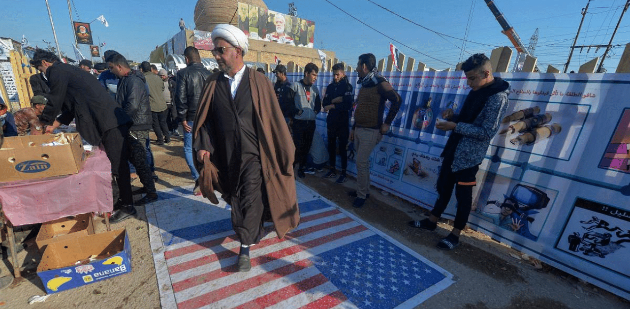 An Iraqi cleric walks on a US flag painted on the ground as people gather to pay respects by the grave of slain commander Abu Mahdi al-Muhandis at the Wadi al-Salam. Credit: AFP Photo