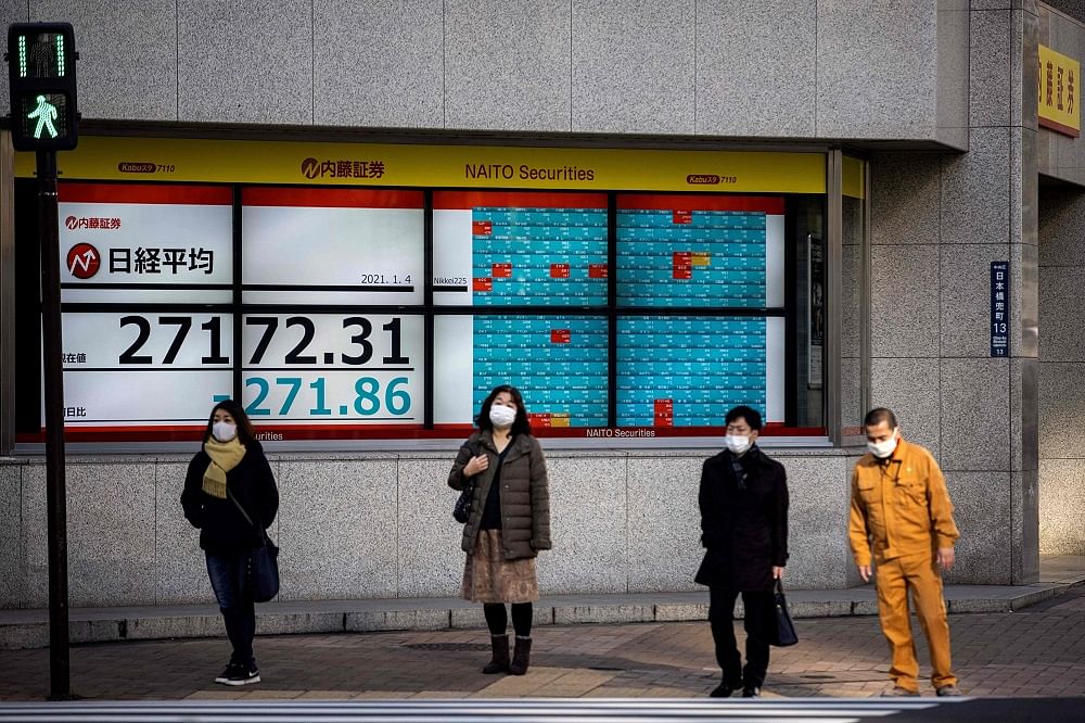 Pedestrians wearing face masks stand next to a stock indicator displaying numbers of Nikkei 225 of the Tokyo Stock Exchange. Credit: AFP Photo