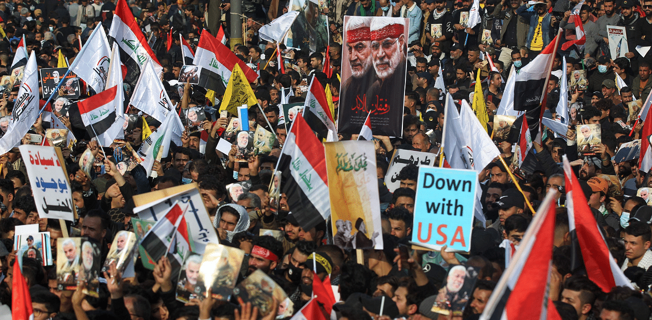  Iraqi demonstrators lift flags and placards as they rally in Tahrir square in the capital Baghdad to mark a year of the killing of Qasem Soleimani. Credit: AFP Photo