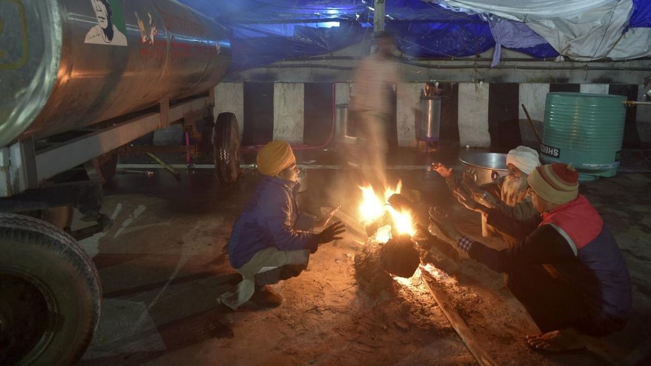 Farmers sit around a bonfire to warm themselves on a cold evening at Delhi-UP Ghazipur border, during their protest against new farm law, in Ghaziabad. Credit: PTI.
