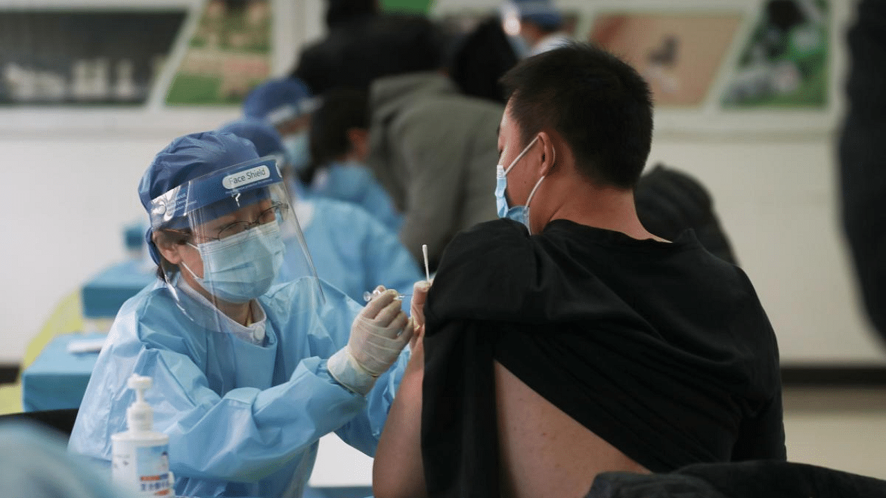 A medical worker (L) administers a Covid-19 coronavirus vaccine to a man at a temporary vaccination centre in Beijing. Credit: AFP File Photo