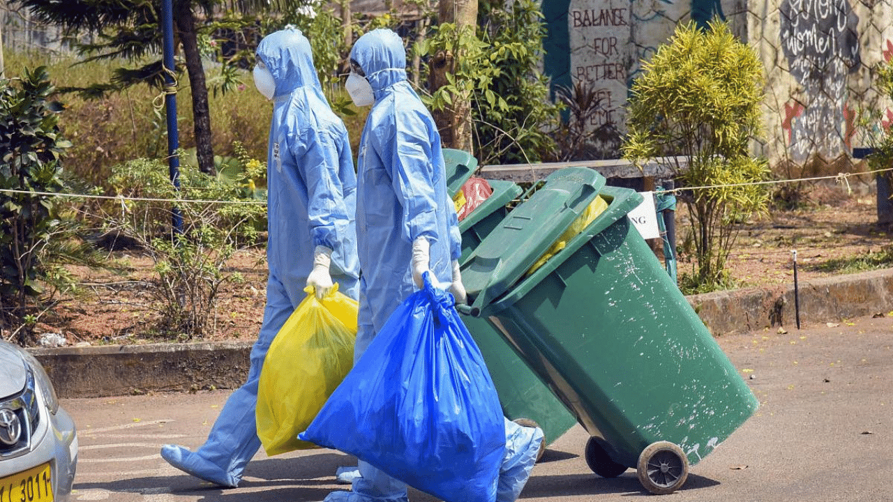 Medical staff, wearing protective suits, hold medical waste as they exit the Special Isolation Ward set up to provide treatment to novel coronavirus patients at Kochi Medical college, in Kerala. Credit: PTI File Photo