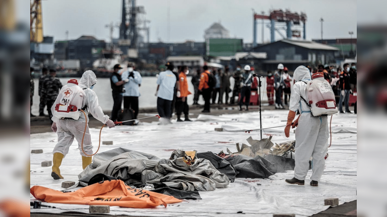 Health workers spray disinfectant over body bags containing human remains recovered from the crash site of Sriwijaya Air flight SJ182 at the port in Jakarta on January 10, 2021, following the January 9 crash of the airline's Boeing 737-500 aircraft into the Java Sea minutes after takeoff. Credit: AFP Photo