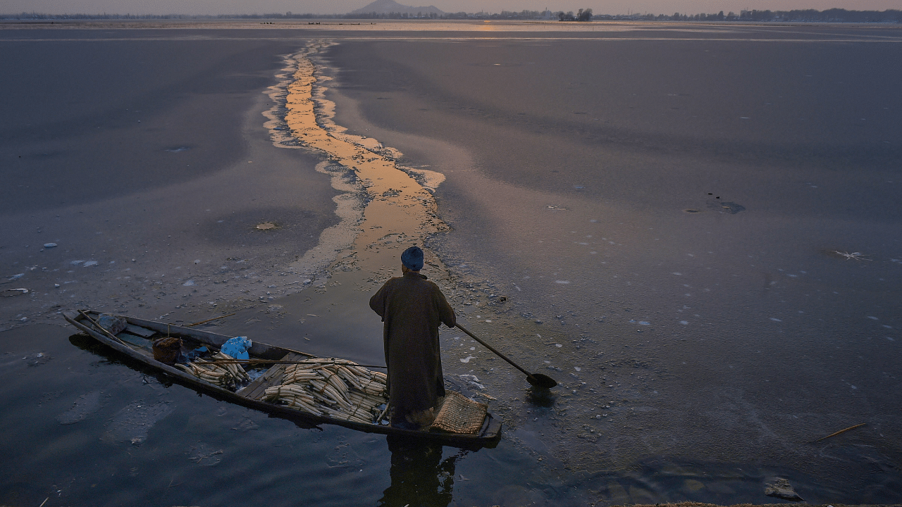 A vegetable vendor row his boat after breaking the frozen surface of Dal Lake, during sunset in Srinagar. Credit: PTI Photo