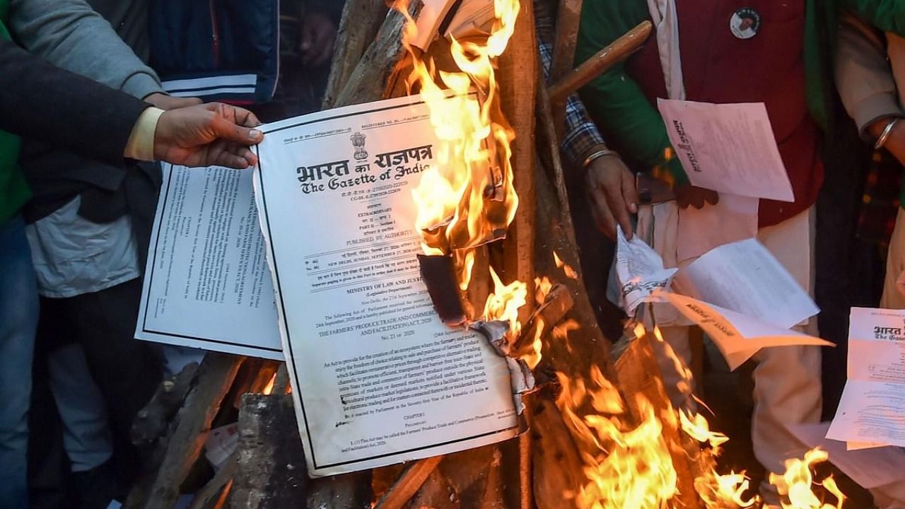 Farmers burn copies of the new farm laws as they celebrate 'Lohri' festival during their ongoing protest against the central government, at Singhu border in New Delhi. Credit: PTI Photo