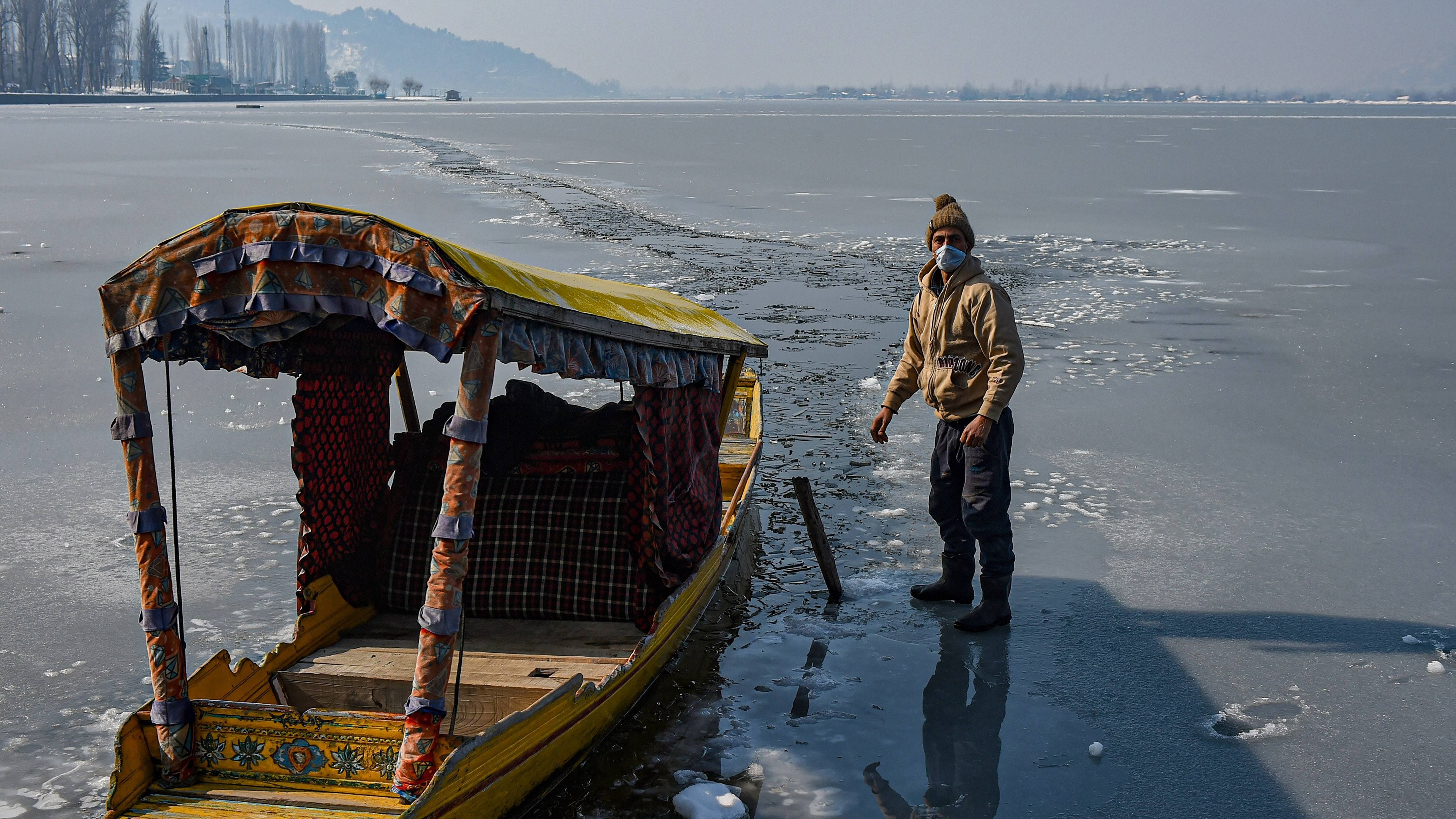 A boatman cuts ice to steer his way on the frozen Dal Lake after the town received fresh snowfall, in Srinagar. Credit: PTI