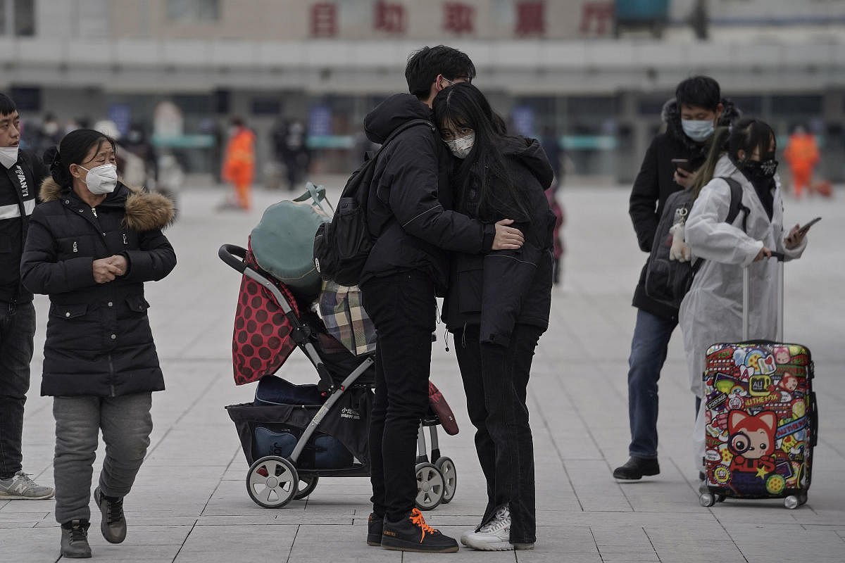 A couple wearing face masks to help curb the spread of the coronavirus embraces each other at the railway station in Beijing. Credit: AP. 