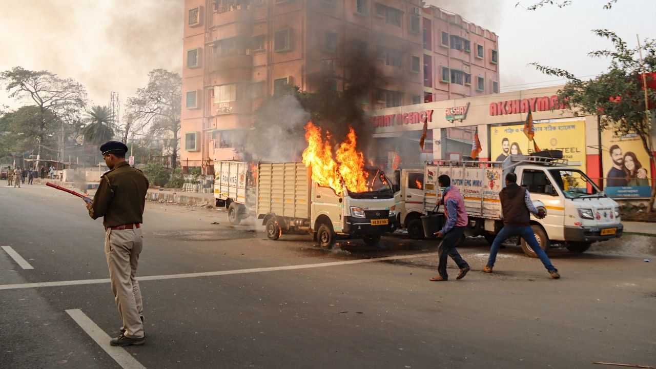 A policeman stands near a burning vehicle, set ablaze allegedly by an irrate mob, near BJP party office in Burdwan district. Credit: PTI Photo