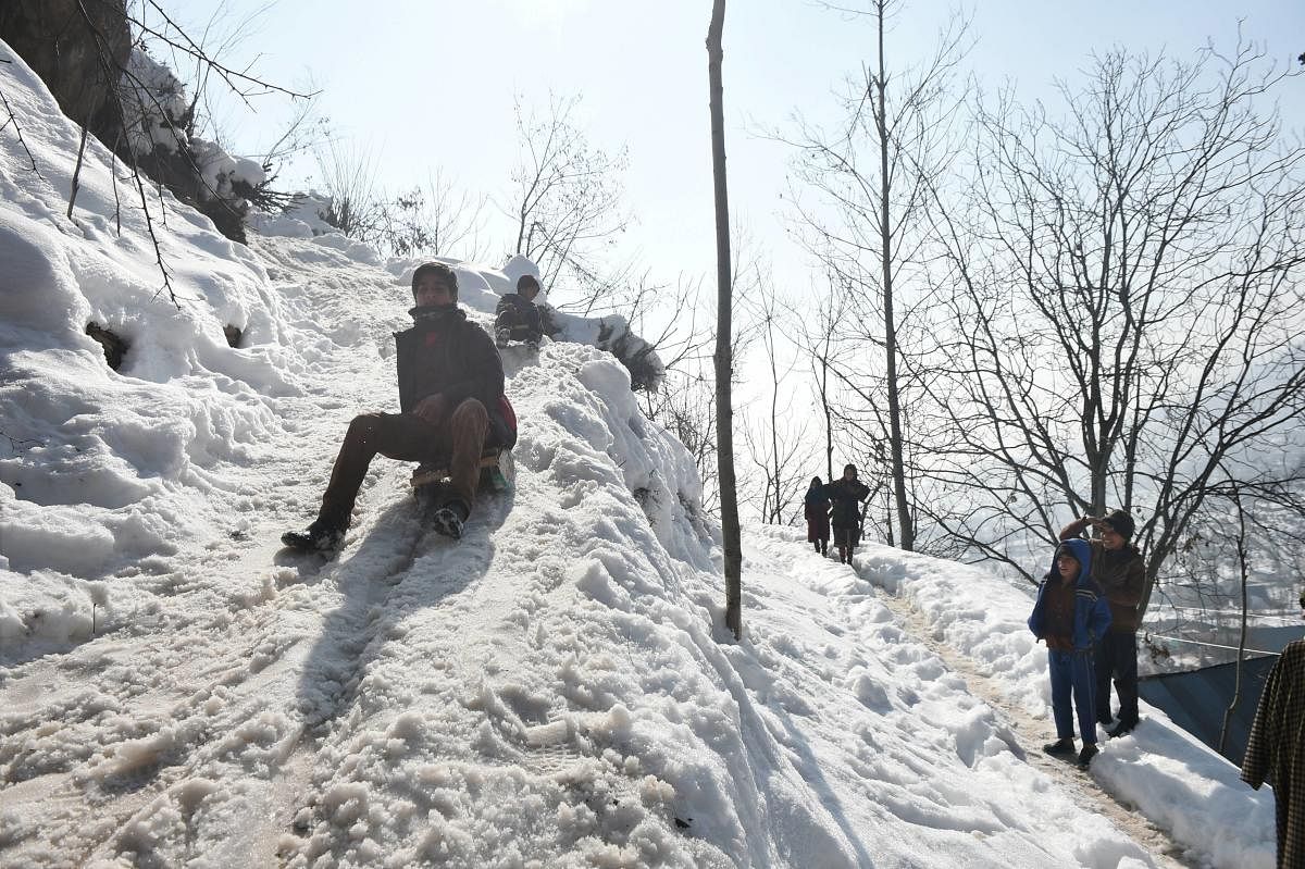 Youngsters play with sledges on a snow laden hilltop after heavy snowfall, on the outskirts of Srinagar. Credit: PTI. 