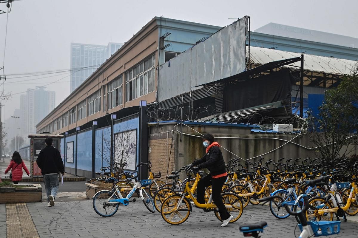 People walk past the closed Huanan Seafood wholesale market in Wuhan, China's central Hubei province on January 23, 2021, one year after the city went into lockdown to curb the spread of the Covid-19. Credit: AFP. 