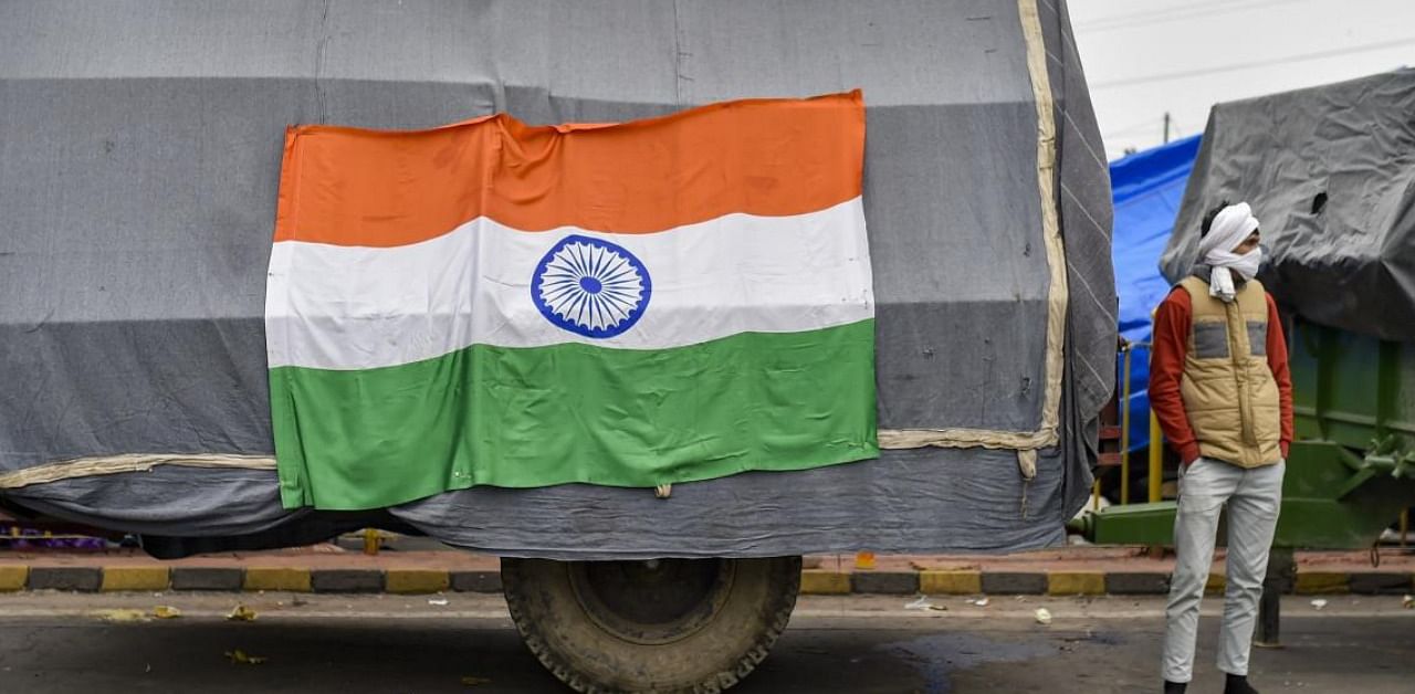  A farmer stands near a tractor trolley with the Tricolor pasted on it, during their ongoing agitation against Centre's farm reform laws, at Ghazipur border in New Delhi, Monday, Jan. 25, 2021. Credit: PTI Photo