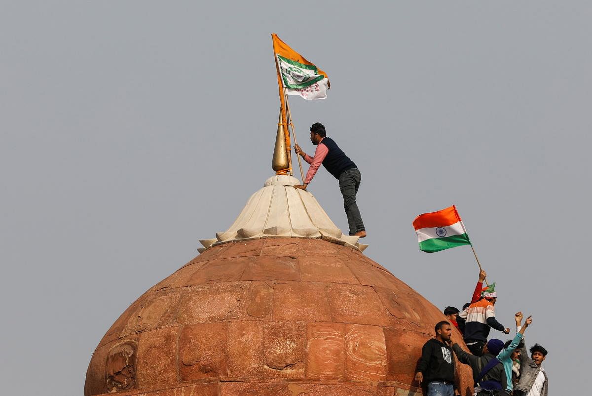 A farmer puts a flag on top of the historic Red Fort, during a protest against farm laws introduced by the government, in Delhi, India, January 26, 2021. Credit: REUTERS