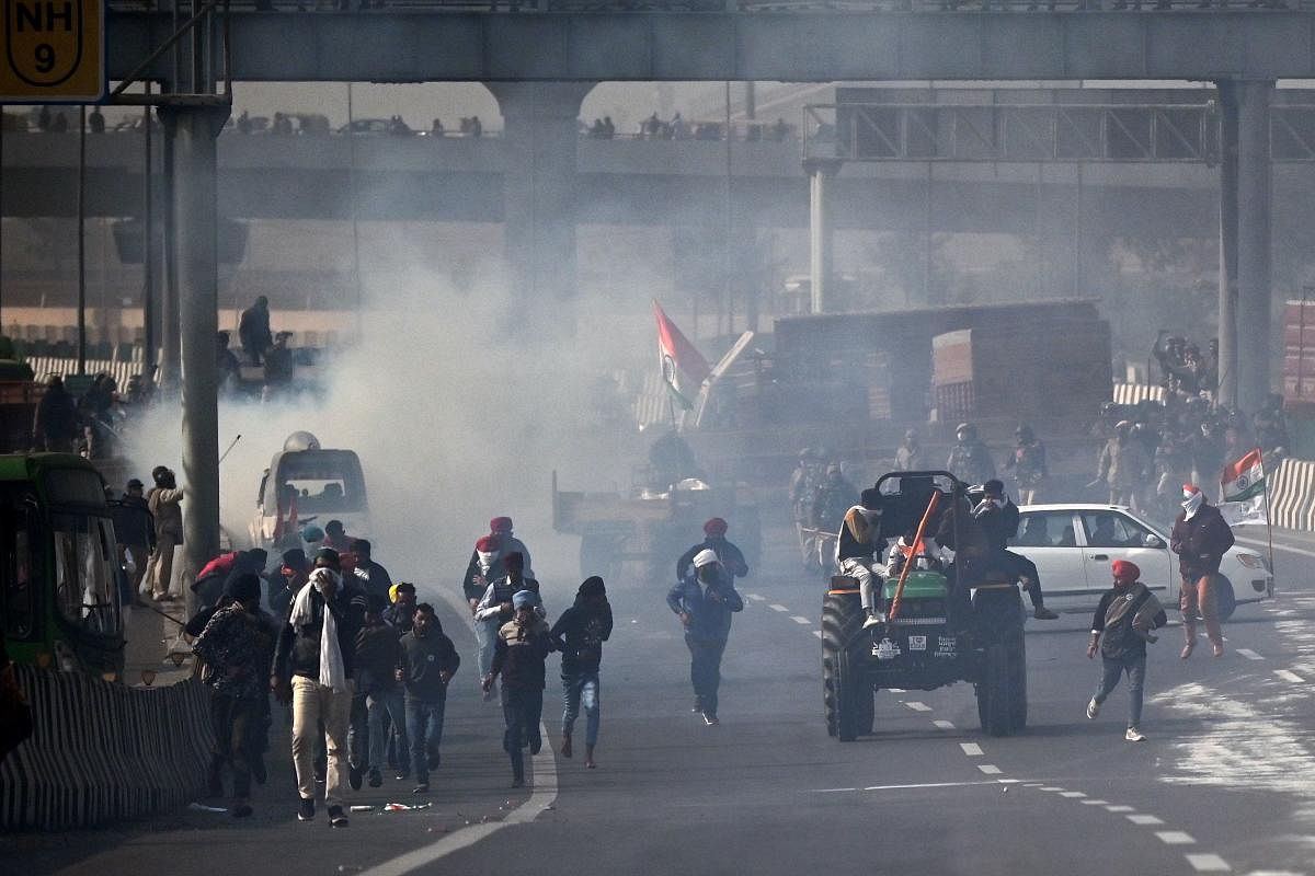Farmers take part in a tractor rally as they ride through the smoke of tear gas fired by the police. Credit: AFP. 