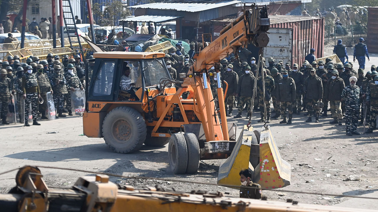 Security forces (back) watch as police sets up road blocks at the Delhi-Haryana state border in Singhu. Credit: AFP Photo