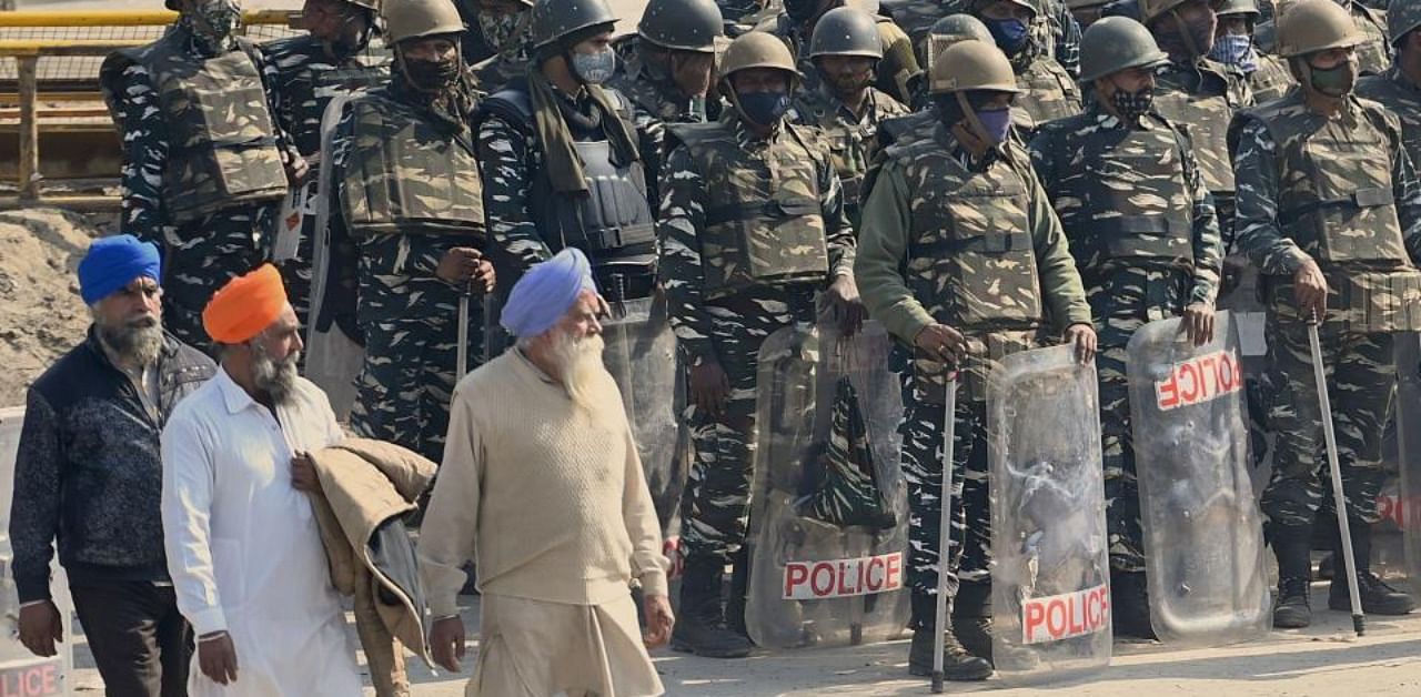Farmers walk past security forces standing guard at Singu border in New Delhi on January 27, 2021, as police closed several main roads. Credit: AFP Photo