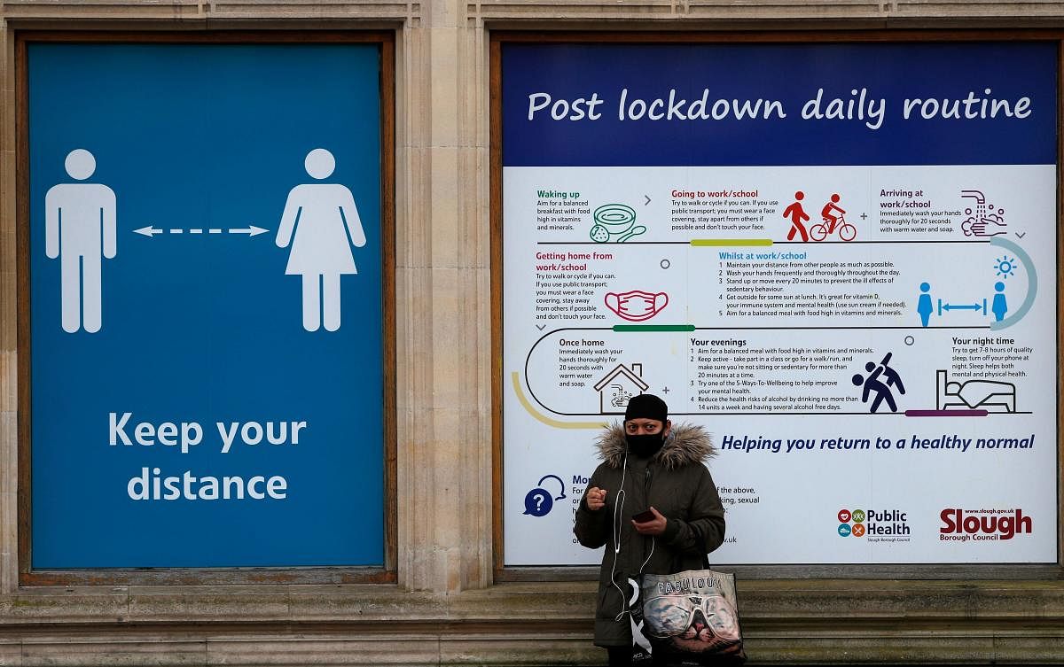 A pedestrian stands next to hoarding with advice on how to stay safe during the Covid-19 pandemic on the high street in Slough, west of London. Credit: AFP. 