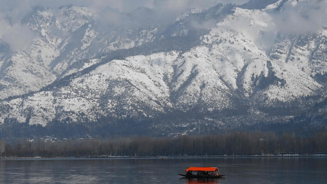 A boat is seen with snow-covered mountains in the background at Dal lake in Srinagar on January 24, 2021. Credit: AFP Photo