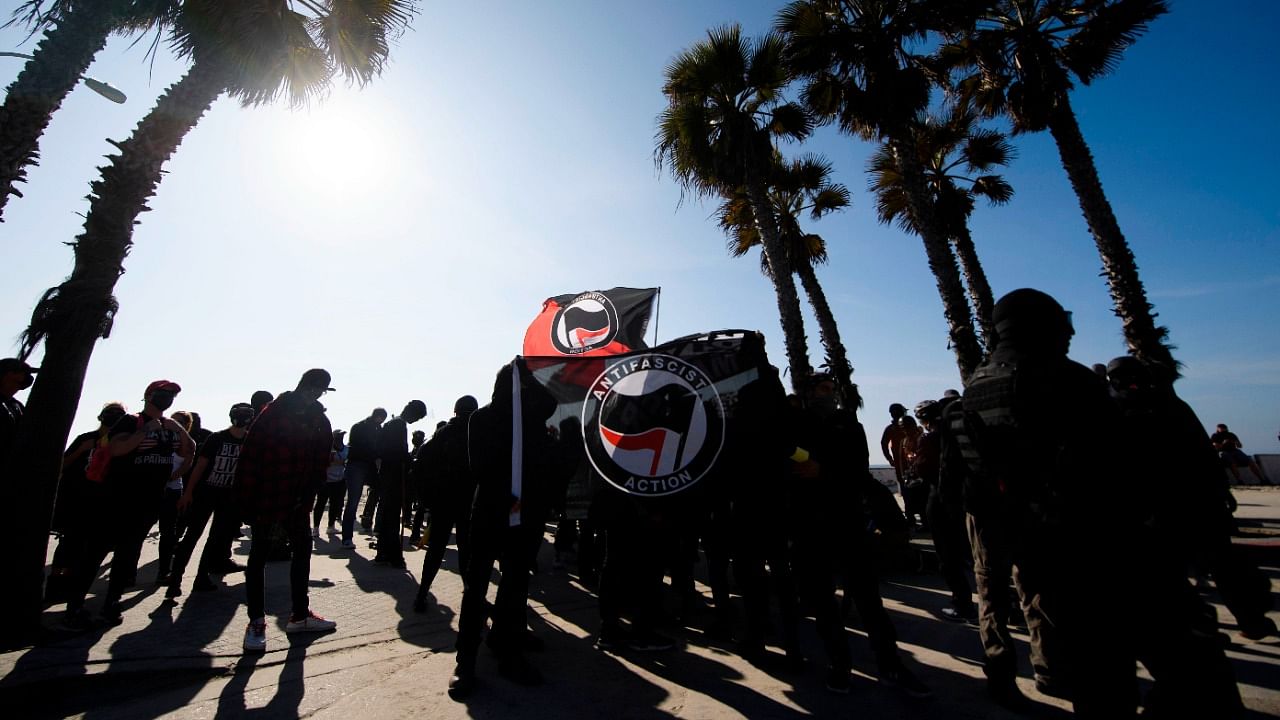 Counter-protesters, some carrying ANTIFA flags, stand beneath palm trees on the beach awaiting to confront demonstrators for a "Patriot March" demonstration in support of US President Donald Trump on January 9, 2021 in the Pacific Beach neighborhood of San Diego, California. Credit: AFP File Photo