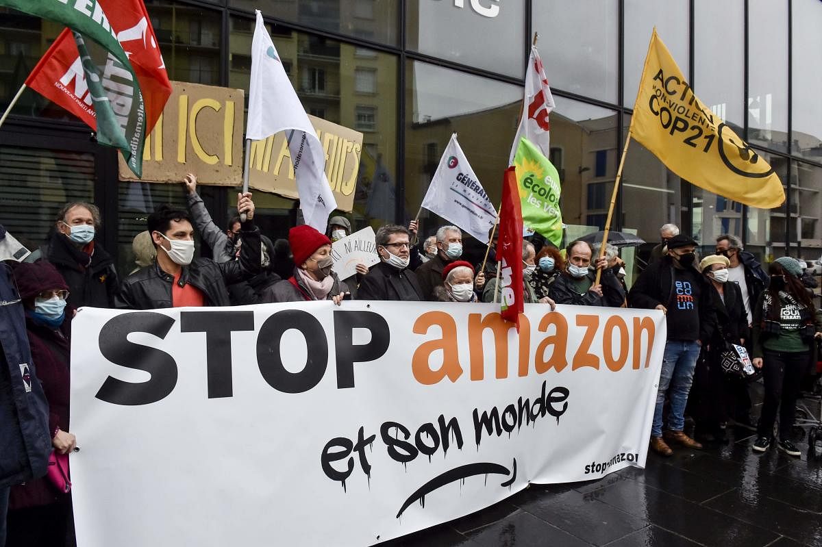 Demonstrators hold a banner reading "Stop Amazon and its world" and wave flags as they gather to protest against Amazon implantation, in front of the Perpignan Mediterranee Metropole headquarters in Perpignan. Credit: AFP. 
