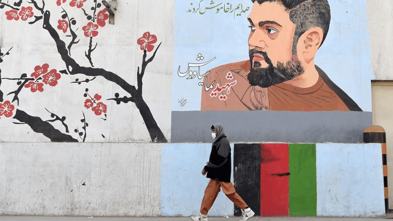 A man walks past a barrier wall painted with an image of former Afghan Tolo TV presenter Yama Siawash, who was killed in a bomb attack on November 7, 2020, along a roadside in Kabul. Credit: AFP Photo