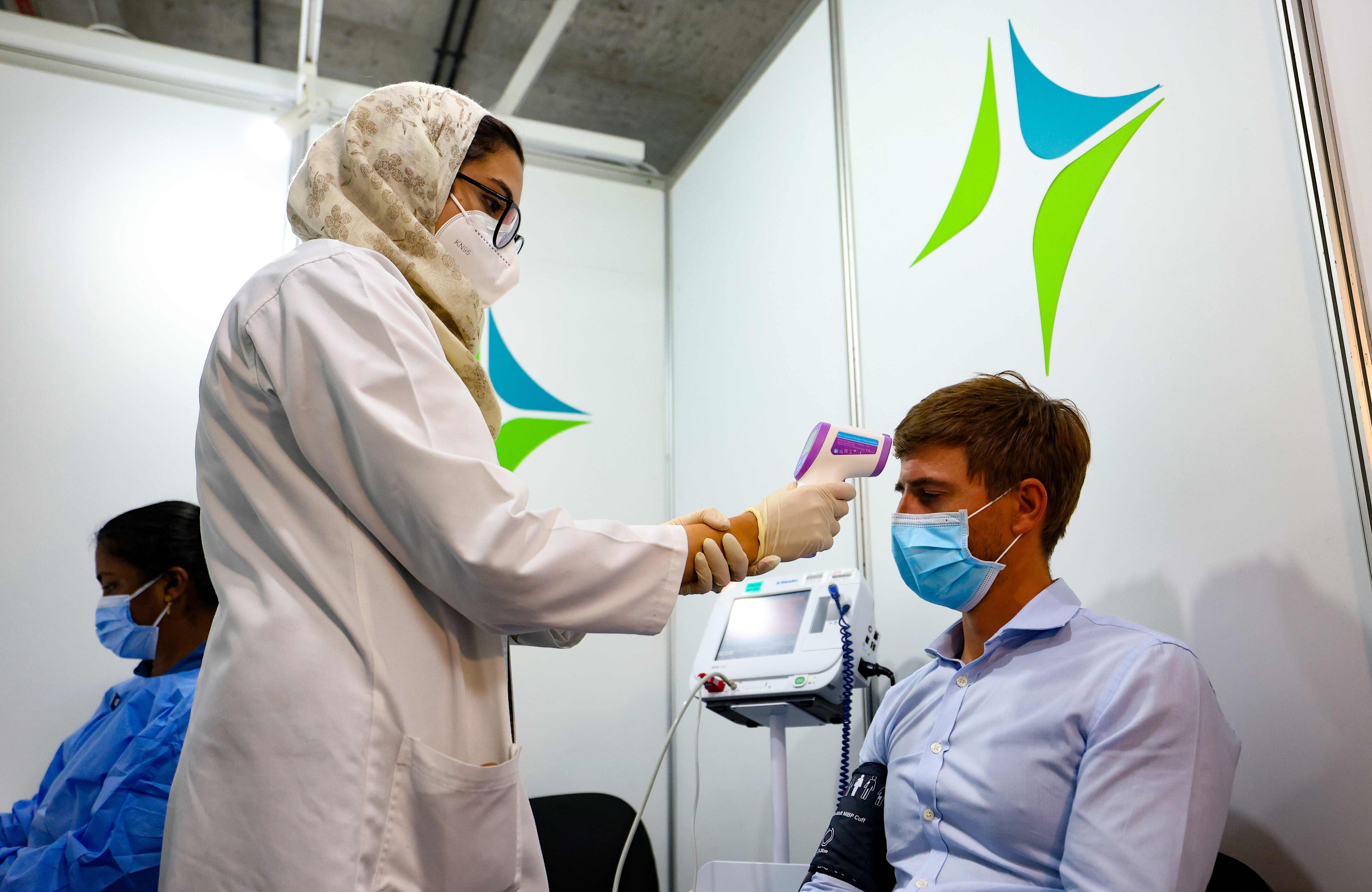 A health worker checks a man's temperature before receiving a dose of vaccine against the coronavirus at a vaccination centre set up at the Dubai International Financial Center in the Gulf emirate of Dubai, on February 3, 2021. - The United Arab Emirates, which includes Dubai and six other emirates, has suffered a spike in cases after the holiday period. It was among the first to launch a vast vaccination campaign in December 2020 for its population of nearly 10 million and has administered at least three million doses to more than a quarter of its population, second only to Israel in the global race, according to the German data agency Statista. Credit: AFP Photo