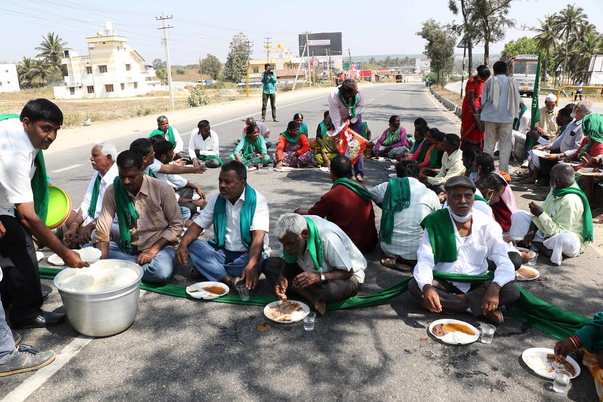 Farmers consume food on highway in Hassan on Saturday. DH PHOTO