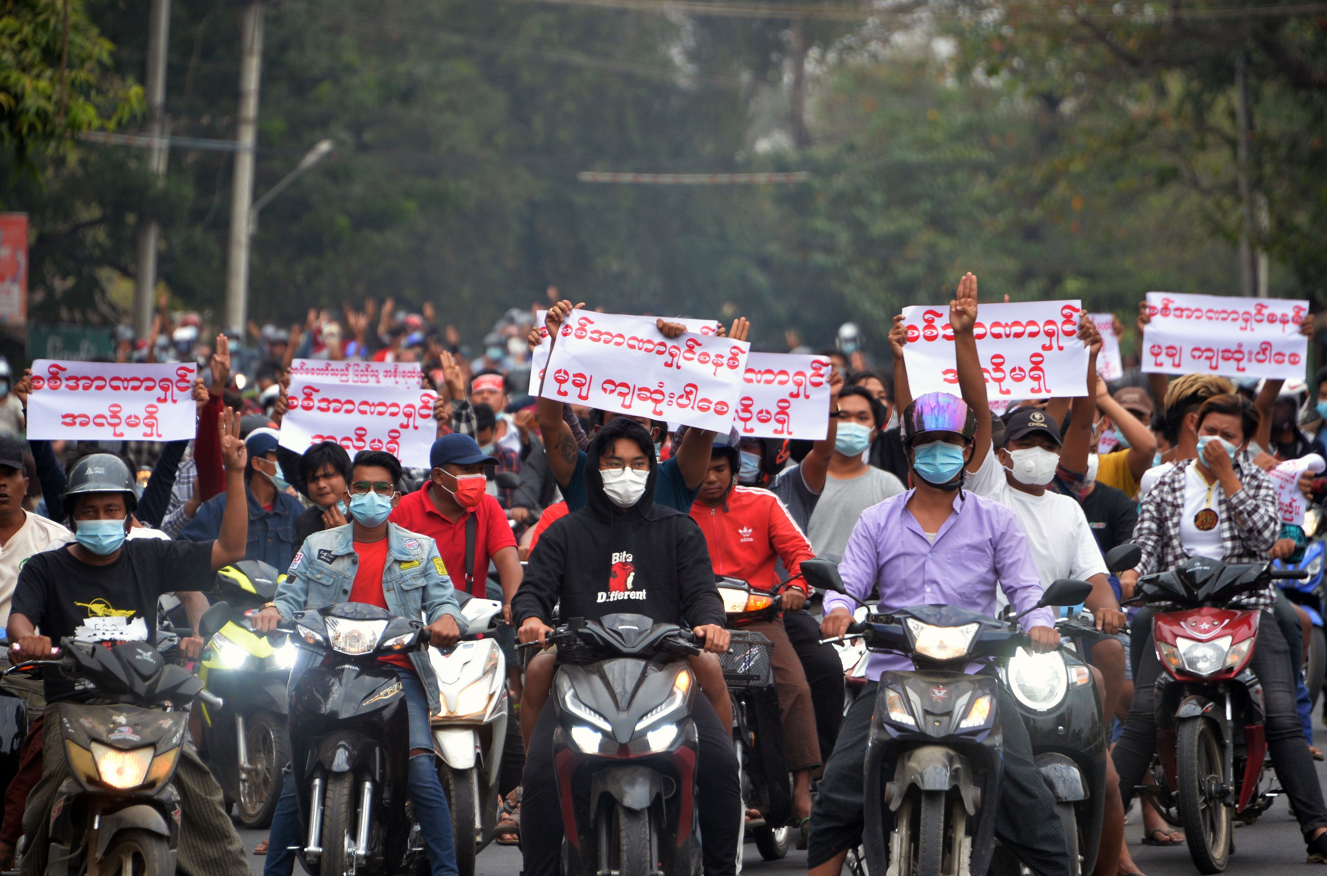 Protesters holding up the three finger salute and signs while riding scooter bikes during a demonstration against the military coup in Naypyidaw. Credit: AFP File Photo