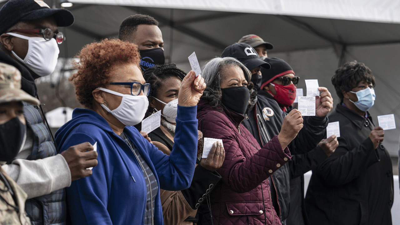 A group of people show off their coronavirus vaccine record cards in the parking lot of Six Flags. Credit: AFP Photo