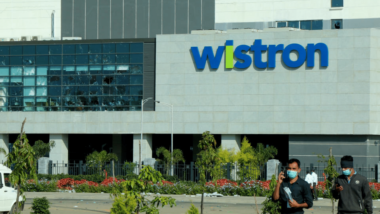 Men wearing protective face masks walk past broken windows of a facility run by Wistron Corp, a Taiwanese contract manufacturer for Apple, in Narsapura near the southern city of Bengaluru, India, December 14, 2020.  Credit: Reuters File Photo