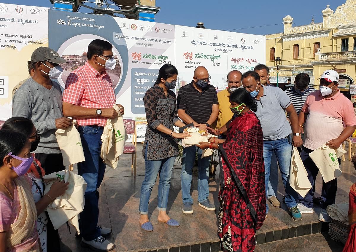 Deputy Commissioner Rohini Sindhuri distributes cloth bags as replacement to plastic bag to a vendor during an awareness programme against plastic, near Devaraja Market in Mysuru on Wednesday. City Corporation Commissioner Gurudatta Hegde is seen. DH PHOT