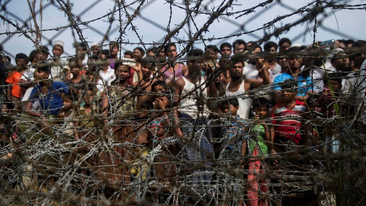 This file photo taken on April 25, 2018 shows Rohingya refugees gathered behind a barbed-wire fence at a temporary settlement setup in a "no man's land" border zone between Myanmar and Bangladesh, near Maungdaw district in Myanmar's Rakhine state. Credit: AFP Photo
