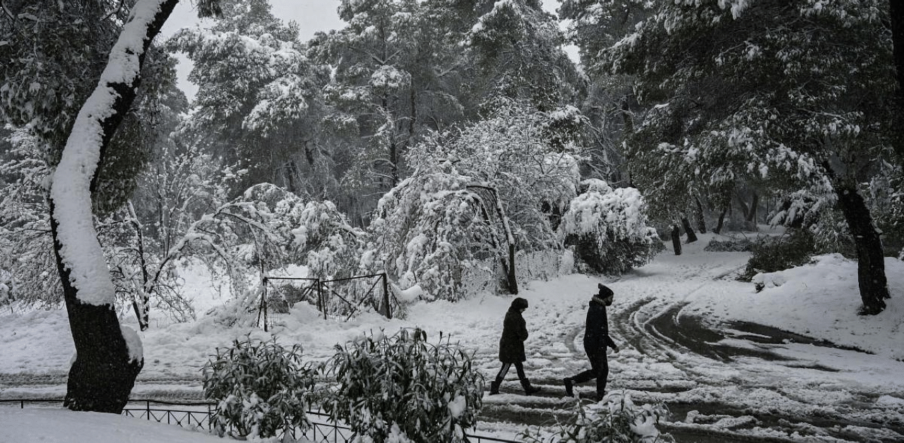 People walk on a snow-covered street during snowfall in a northern suburb of Athens. Credit: AFP Photo