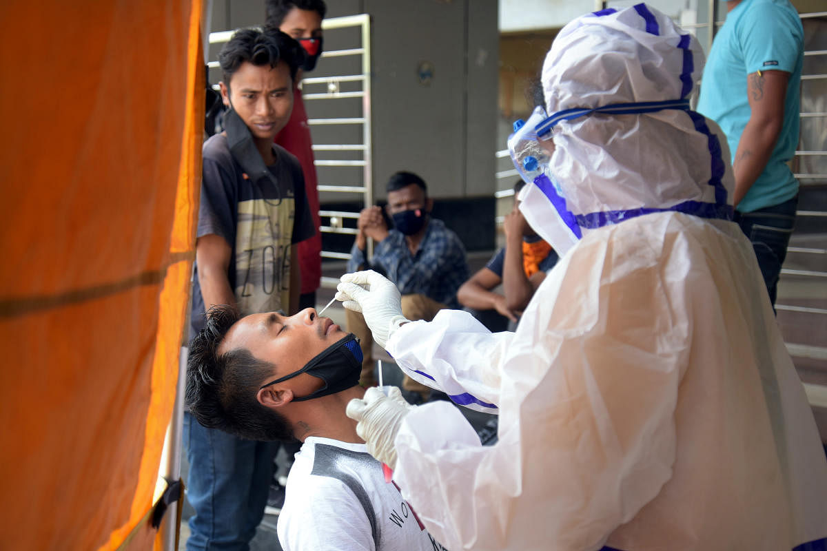 A health worker takes swab of a passenger for a coronavirus test upon his arrival at satellite bus stand on Mysuru Road, in Bengaluru on Wednesday. DH Photo/Pushkar V