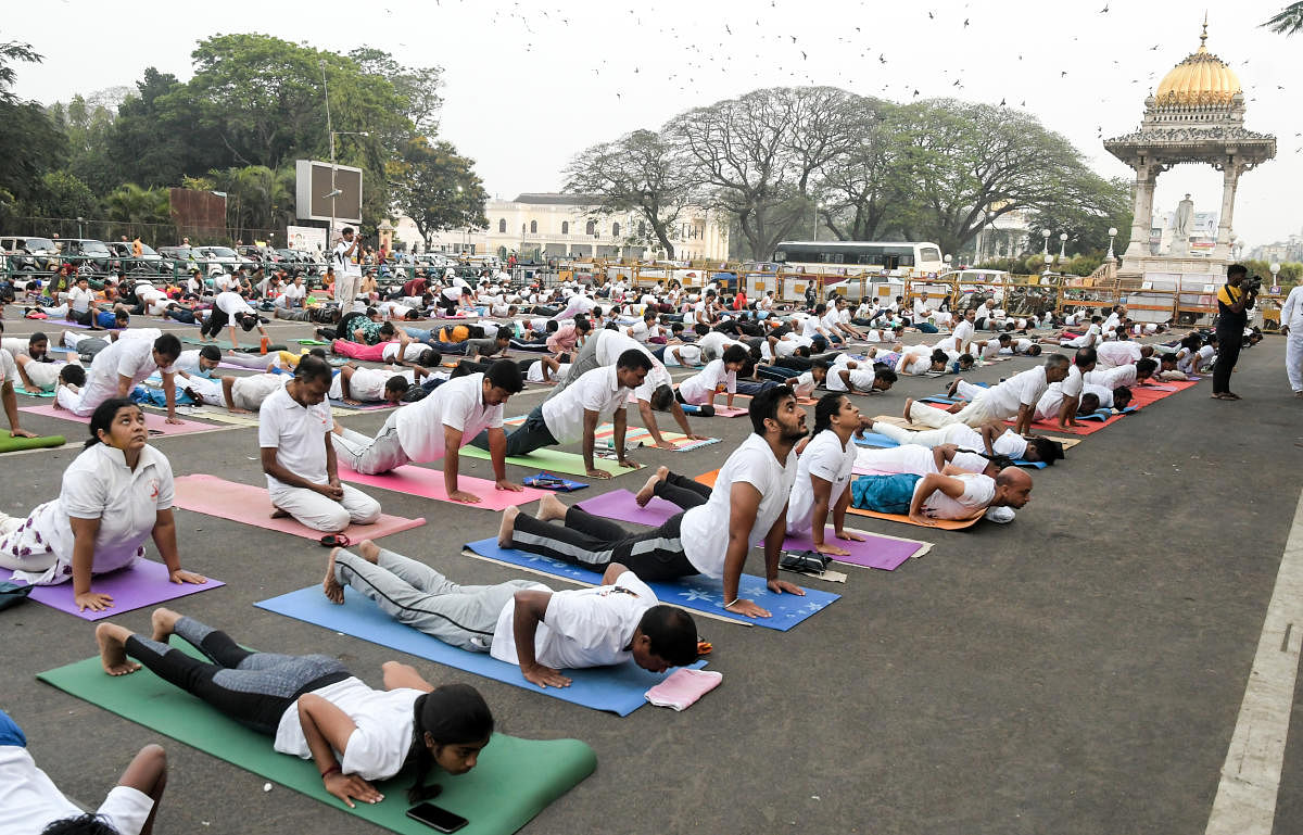 Yoga enthusiasts demonstrate Surya Namaskara near Kote Anjaneya Swamy temple, Mysuru Palace on Friday. DH Photo