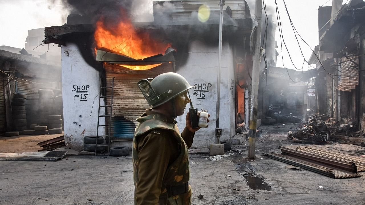 A security official stands in front of a burning shop following clashes over the new citizenship law, in Gokulpuri area of northeast Delhi, Wednesday, February 26, 2020. Credit: PTI Photo