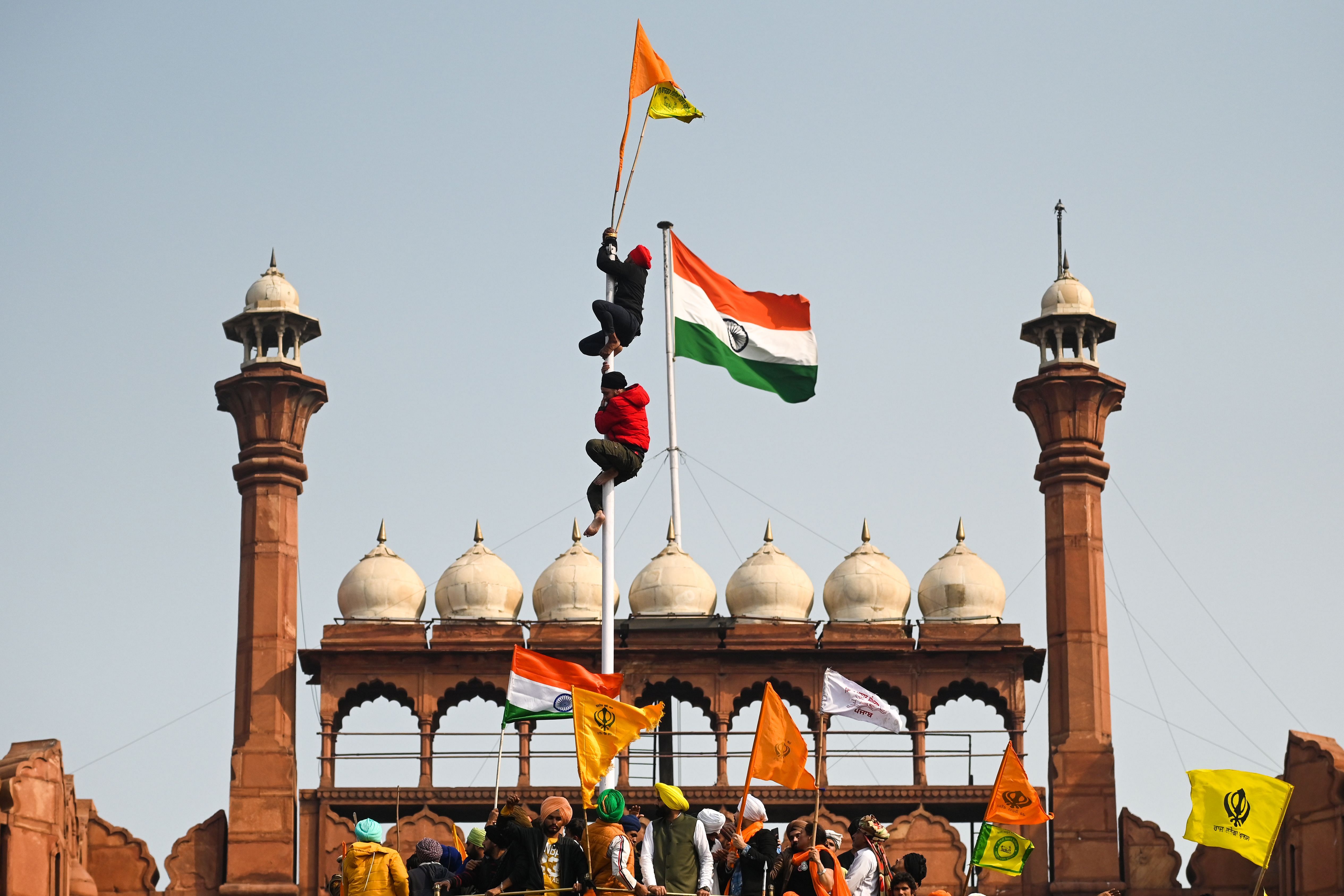 Protesters climb a flagpole at the ramparts of the Red Fort as farmers continue to demonstrate against the central government's recent agricultural reforms in New Delhi on January 26, 2021. Credit: PTI Photo