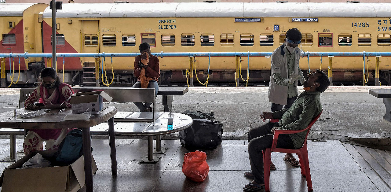 A health worker (top R) takes a nasal swab of a passenger for a Covid-19 test upon his arrival at at the Yeshwanthpur Railway Station, in Bengaluru. Credit: AFP Photo