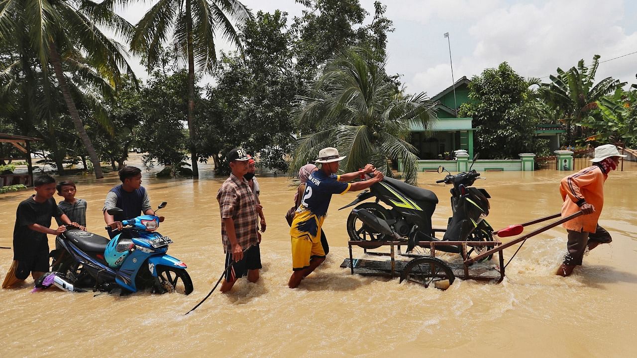 People push their motorcycles through an area flooded after the embankment of Citarum River burst, in Bekasi, Indonesia. Credit: AP/PTI Photo