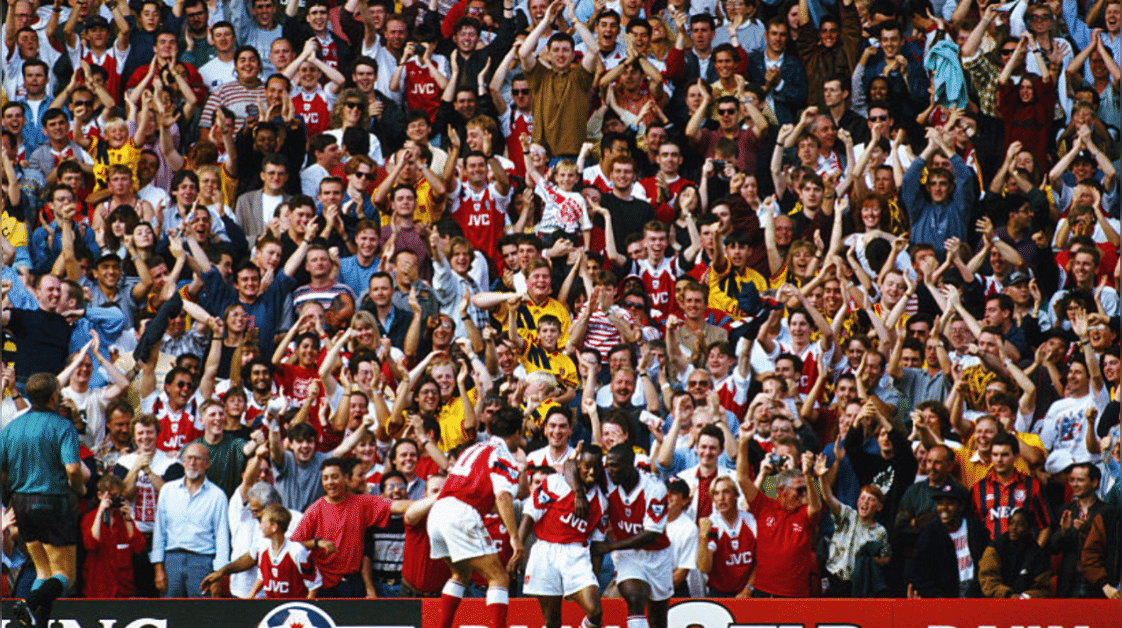 Arsenal Fans in the North Bank celebrate the second of Ian Wright two goals as a lone Everton fan (bottom right, striped red/ blue shirt) looks on during the FA Premier League match between Arsenal and Everton at Highbury on August 28, 1993 in London, England. Credit: Getty Images