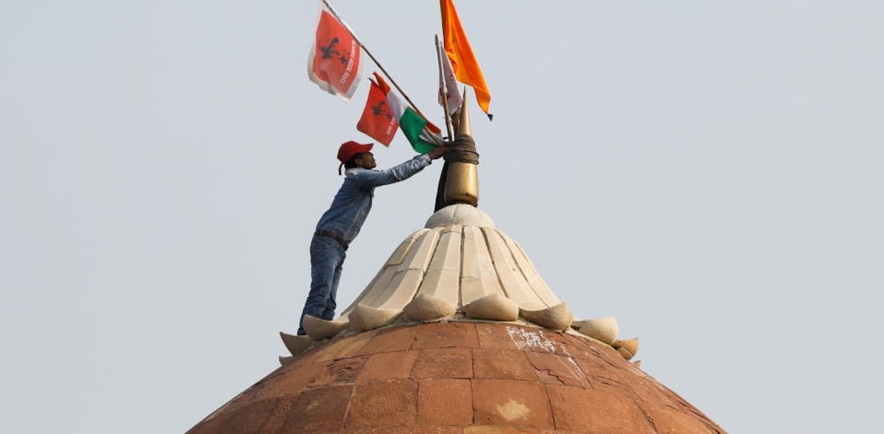A man holds a flag as he stands on the top of the historic Red Fort during a protest against farm laws introduced by the government, in Delhi, India, January 26, 2021. Credit: Reuters Photo